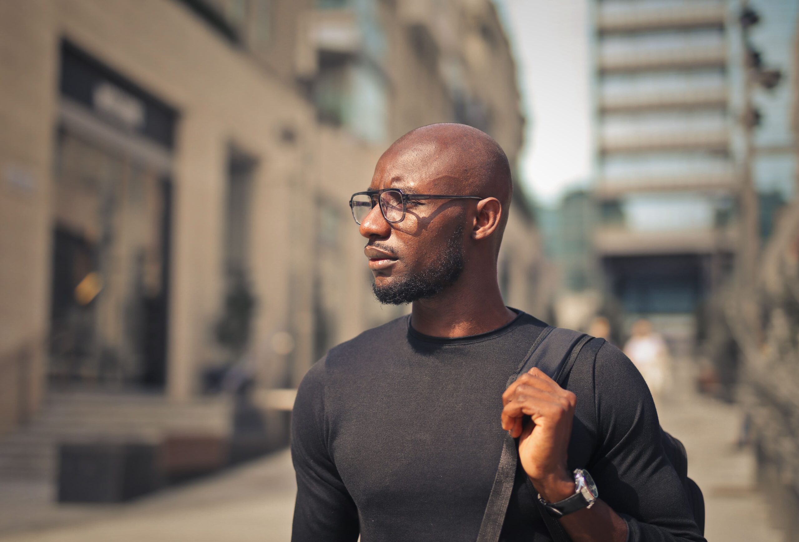 young man with glasses wearing black t shirt backpack street